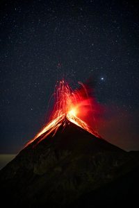 A volcano erupts with magma in front of a starry sky