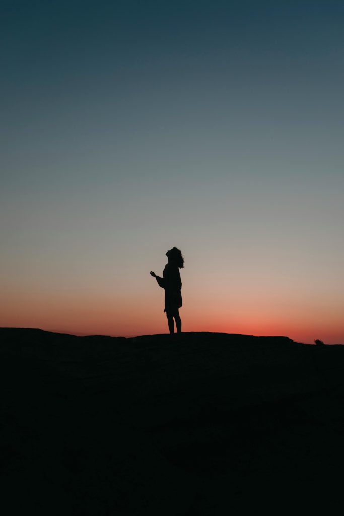 A silhouette of a woman looks up at the sky at twilight