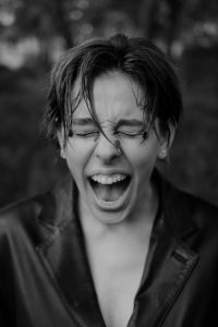 A person with short, disheveled hair screams with their eyes pressed tightly closed