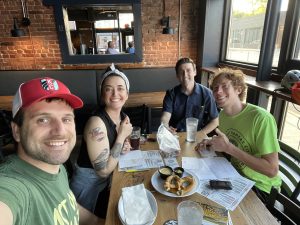 Seated at a restaurant, Briana Anderson, local activists, and KC Councilmember Eric Bunch send postcards encouraging locals to vote on behalf of the Climate Changemakers’ Kansas City chapter. Photo Credit: Briana Anderson