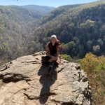 Taking time for self-care, Briana Anderson sits perched on a stone overhang surrounded by the autumnal mountains of Arkansas. Photo Credit: Briana Anderson