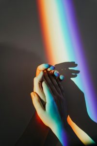 Two hands join, illuminated by a prismatic ray of light. Photo Credit: Cottonbro Studio